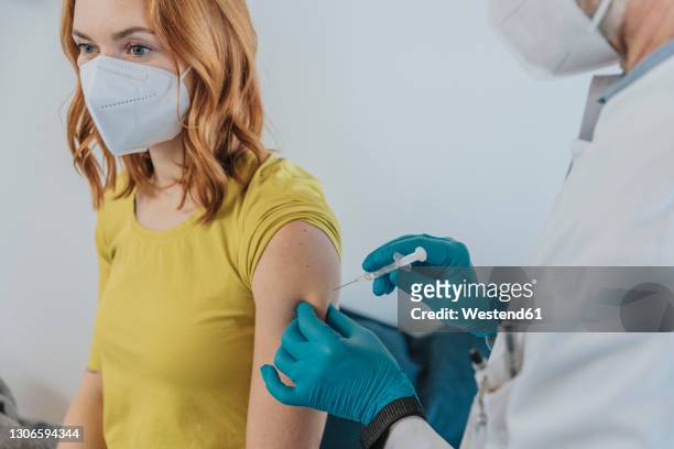 doctor injecting covid-19 vaccination on patient hand while standing at examination room - covid 19 vaccine stock pictures, royalty-free photos & images