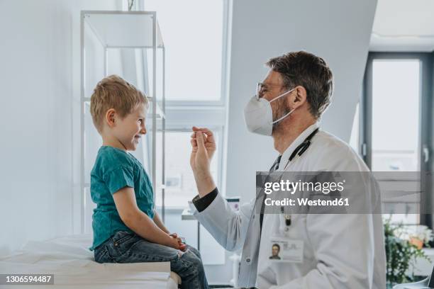 pediatrician wearing protective face mask taking nasal swab test of boy while standing at clinic - pediatrician covid stock pictures, royalty-free photos & images