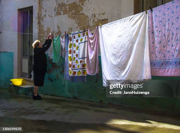 ragusa, sicily: senior woman hanging colorful sheets - ragusa sicily stock pictures, royalty-free photos & images