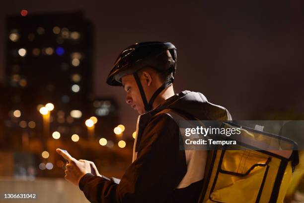 delivery rider at dusk looking at the smartphone. - bike messenger stock pictures, royalty-free photos & images