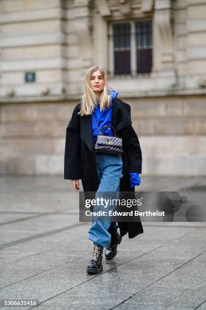 Xenia Adonts wears sunglasses from Linda Farrow, a black long wool coat, a bold blue hoodie sweater from Cherry LA, a black leather quilted Chanel...