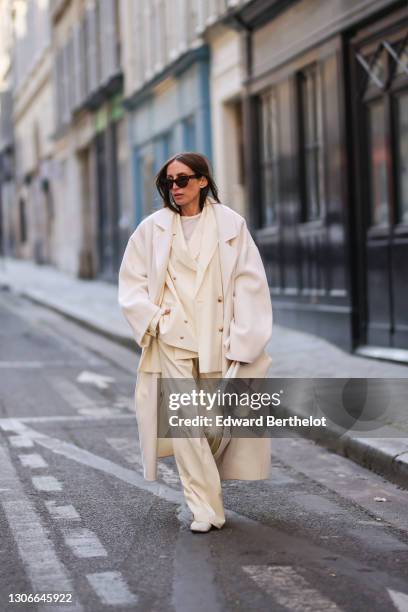 Chloe Harrouche @louloudesaison wears sunglasses, a full Loulou Studio look made of a white oversize wool long coat, a white t-shirt, a cream-color...