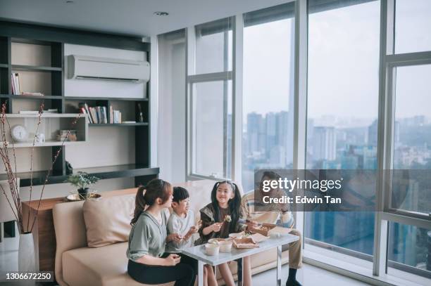 aziatische chinese jonge familie die van het nemen van voedsel voor tv in woonkamer tijdens weekend geniet - apartment living asian stockfoto's en -beelden