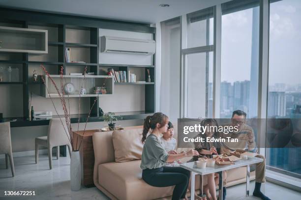 asian chinese young family enjoying take out food in front of tv in living room during weekend - air conditioner family stock pictures, royalty-free photos & images