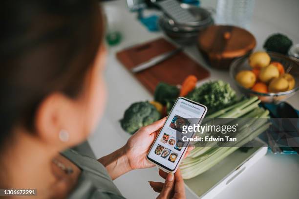 main asiatique de femme chinoise de vue d’angle élevé sur l’application mobile pour la livraison en ligne de nourriture devant le compteur de cuisine - shopping smartphone photos et images de collection