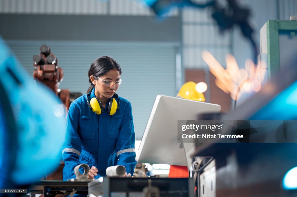 Female Industrial engineer working on desktop computer in robotic welding testing area of research and development in automobile industry. Productivity improvement concepts.