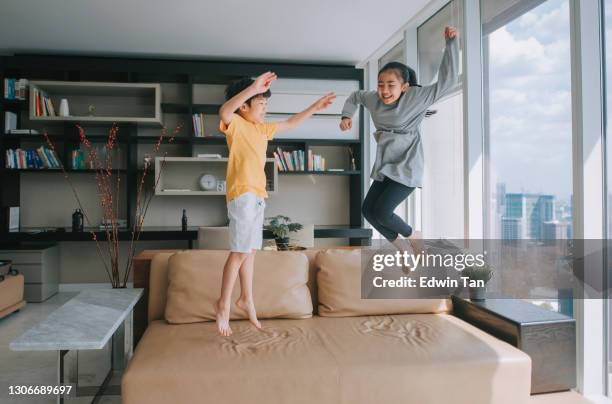 asian chinese young boy and girl jumping on the couch sofa happily - air conditioner family stock pictures, royalty-free photos & images