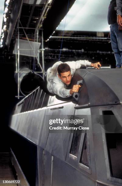 American actor Tom Cruise as Ethan Hunt, filming a scene for the movie 'Mission: Impossible' at Pinewood Studios, 1995. In this scene he clings to a...