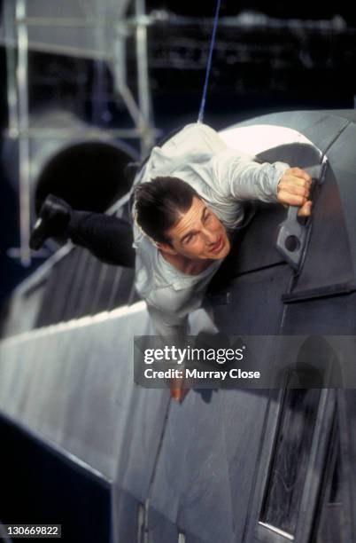 American actor Tom Cruise as Ethan Hunt, filming a scene for the movie 'Mission: Impossible' at Pinewood Studios, 1995. In this scene he clings to a...