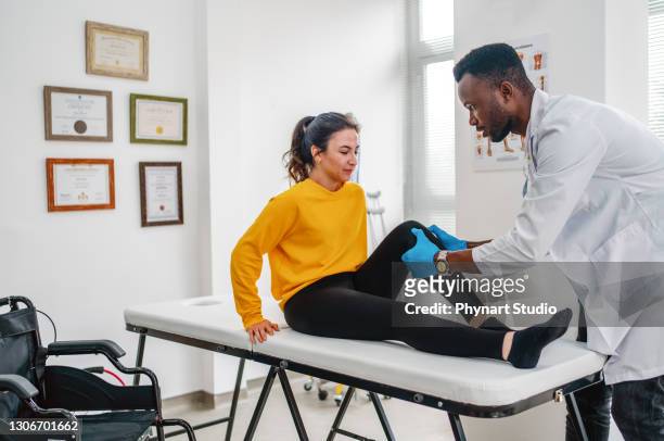 therapist treating injured knee of athlete female patient in clinic - male knee stock pictures, royalty-free photos & images