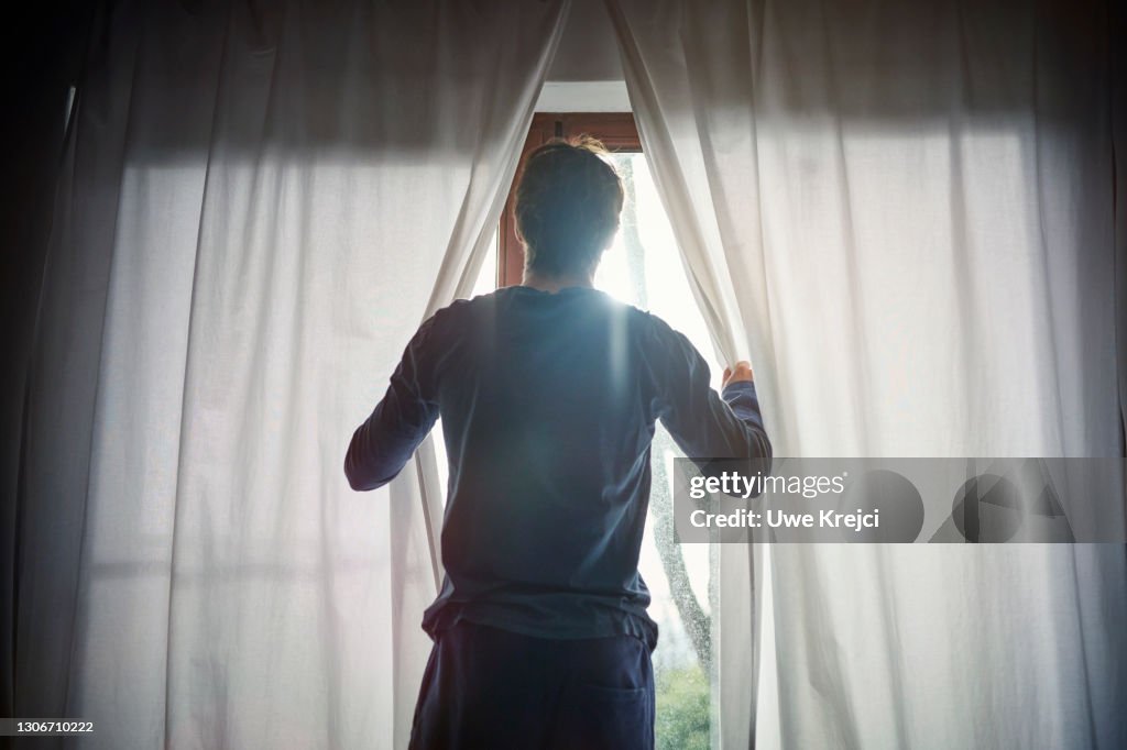Man opening curtains in bedroom