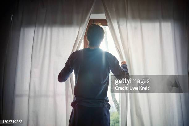 man opening curtains in bedroom - sonnenlicht stock-fotos und bilder