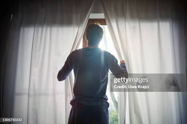 man opening curtains in bedroom - morning foto e immagini stock