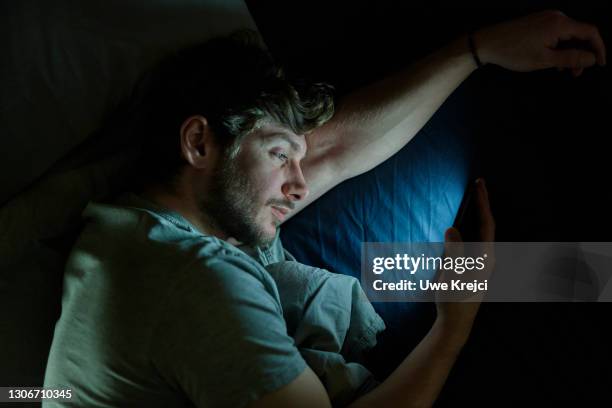 man in bed on smartphone - abhängigkeit stock-fotos und bilder