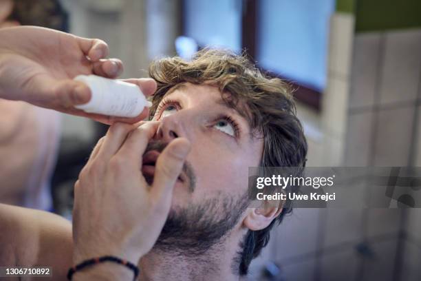man applying eye drops to his eye - augentropfen stock-fotos und bilder