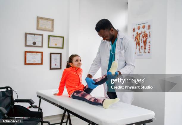 cute little girl lying down on gurney stretching her leg with help of unrecognizable physical therapist - leg stretch girl stock pictures, royalty-free photos & images