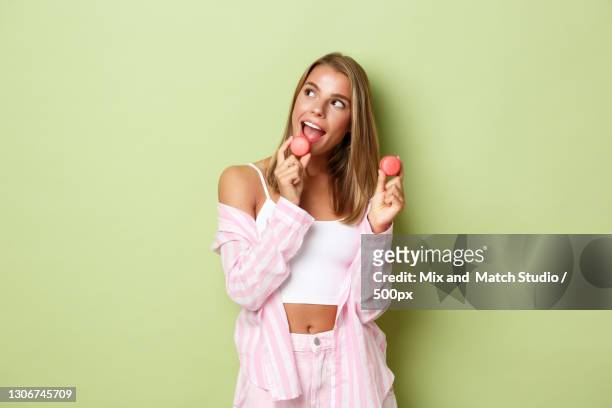 portrait of smiling young woman eating granny smith apple while standing against pink background - glamourous granny 個照片及圖片檔