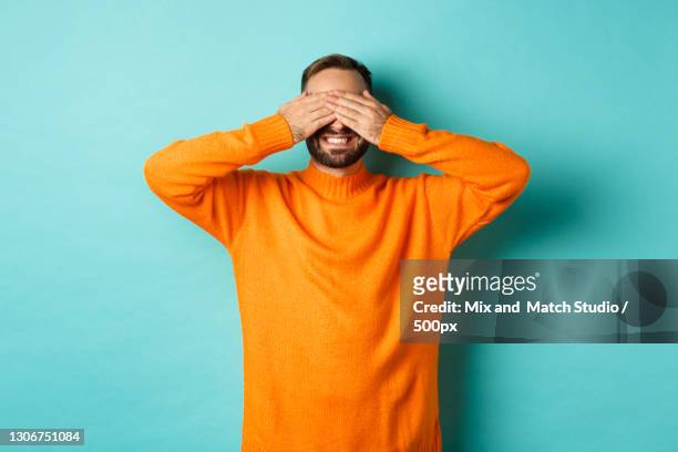 young man covering face with hands while standing against blue background - tierohr stock-fotos und bilder