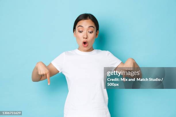 portrait of shocked young woman standing against blue background - looking down stock-fotos und bilder