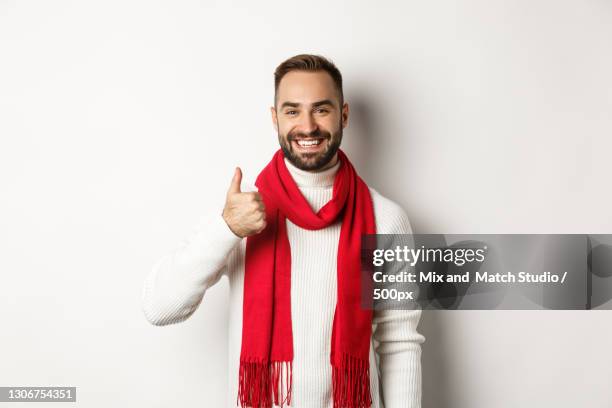 portrait of smiling young man wearing suit while standing against white background - red scarf stock-fotos und bilder