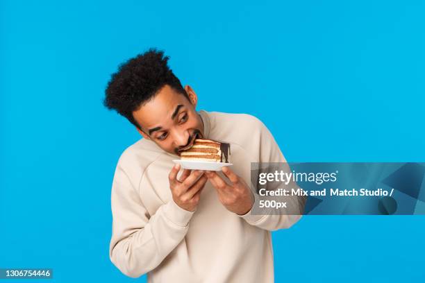 portrait of smiling young man holding donut against blue background - shawl stock pictures, royalty-free photos & images