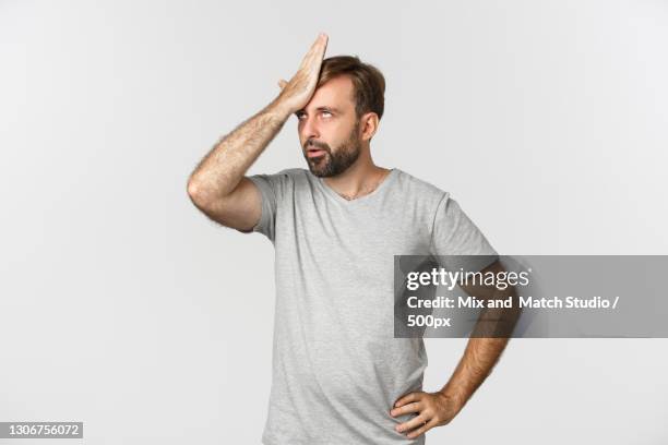 young man with hand on hip standing against white background - slapping face stock pictures, royalty-free photos & images