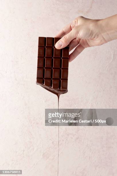 cropped hand of woman holding chocolate bar against wall - chocolate bar stock-fotos und bilder