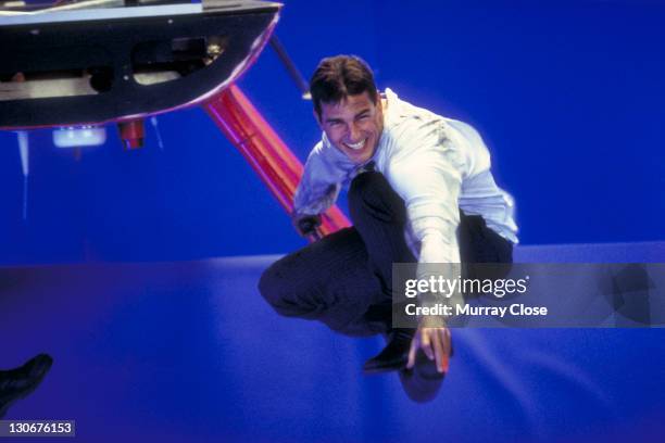 American actor Tom Cruise perches on a helicopter skid against a bluescreen, whilst filming a scene for the movie 'Mission: Impossible' at Pinewood...