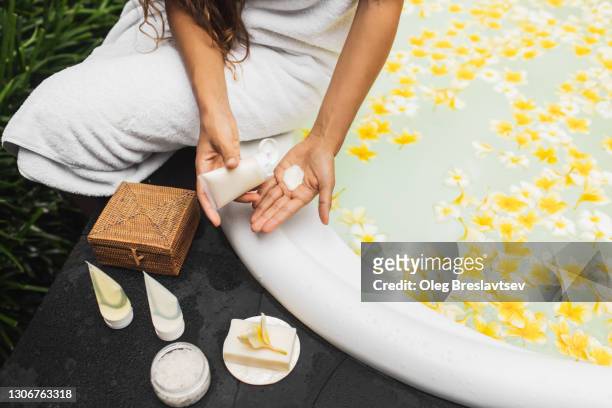 woman squeezing the cream out of the tube on hand and sitting near bath tub. unrecognizable person. - bath salt ストックフォトと画像