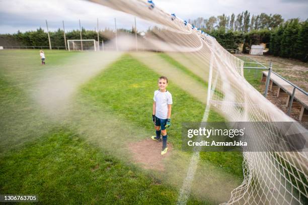 portrait of smiling young boy footballer guarding goal - boy goalie standing in front of goal net stock pictures, royalty-free photos & images