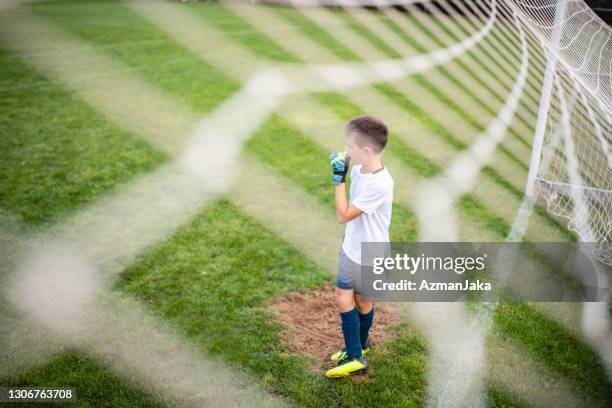 young boy footballer standing at goal waiting for action - boy goalie standing in front of goal net stock pictures, royalty-free photos & images