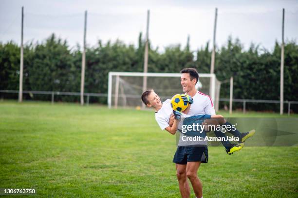 playful coach carrying 8 year old footballer - boy goalie standing in front of goal net stock pictures, royalty-free photos & images