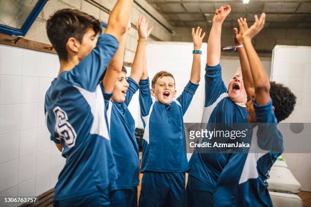 porträt der jubelnden blauen team-fußballer in locker room - fußballtrikot stock-fotos und bilder