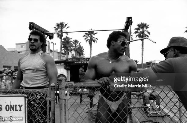 Two men show off their muscles while working out at Muscle Beach in the Venice weight pen circa 1988 in Venice, California.