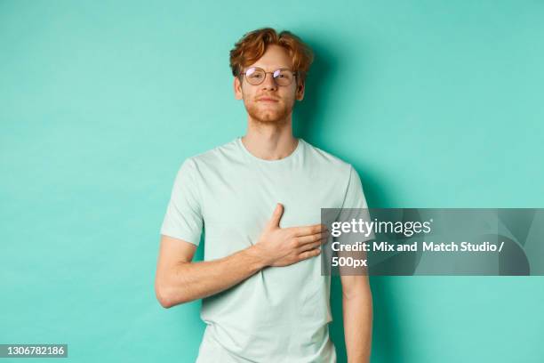 young man wearing sunglasses while standing against blue background - hand aufs herz stock-fotos und bilder