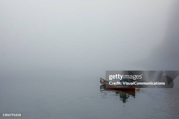 man canoeing on calm lake in moody and sulky weather. - unusual stock pictures, royalty-free photos & images