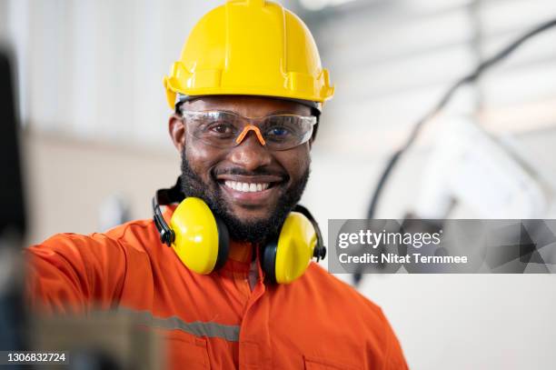 portrait of african engineer with robot in robotics research in automotive industry. reduce costs and reduce working time. productivity improvement concepts. - steel worker stock pictures, royalty-free photos & images