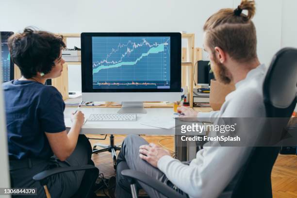 deux collègues analysant un diagramme financier sur un ordinateur - trading desk photos et images de collection