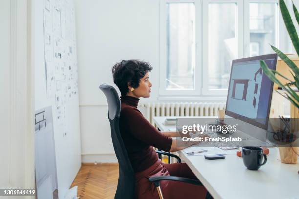 vista laterale di una bellissima designer femminile che lavora a un progetto nel suo ufficio - computer mockup foto e immagini stock