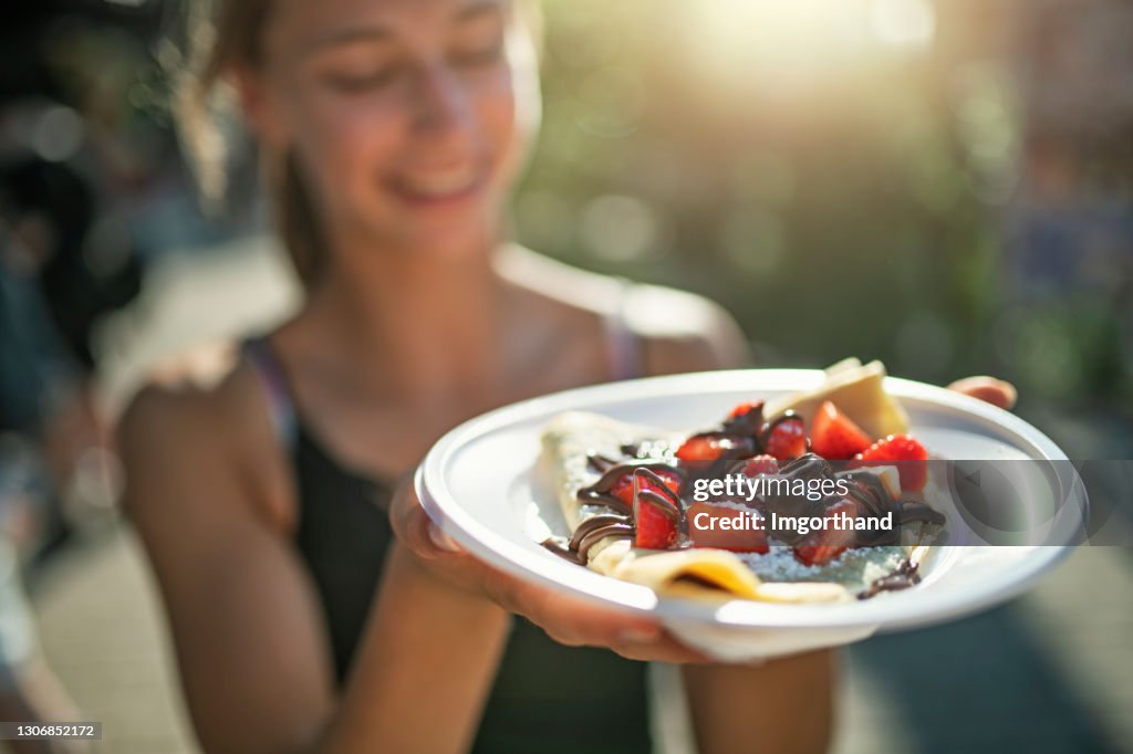 Teenage girl holding a plate with crepe bought at street food stand