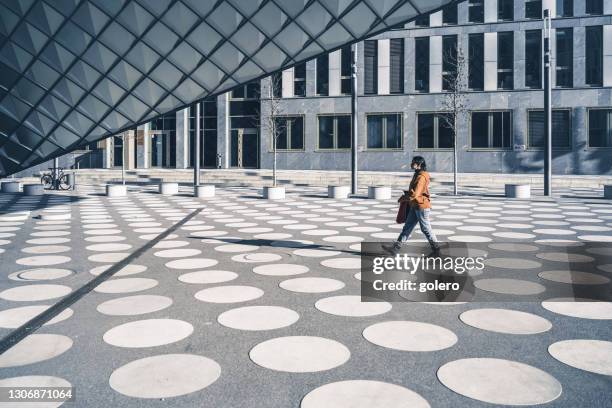 girl in orange hoody walking over white spotted town square in modern berlin - modern town square stock pictures, royalty-free photos & images