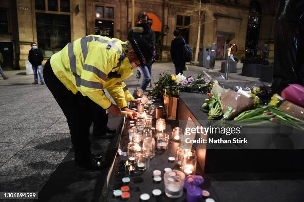 Female police officer lights a candle next to a makeshift memorial during a vigil for Sarah Everard, following her kidnap and murder, on Market...