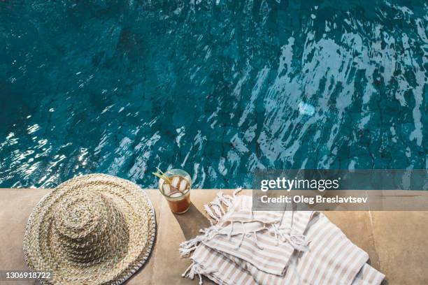 cold summer poolside drink with ice, straw hat and towel near swimming pool - travel service stockfoto's en -beelden