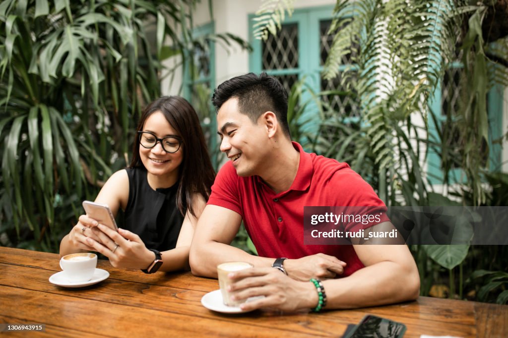 Beautiful adult couple at restaurant shopping online while man holds credit card both smiling