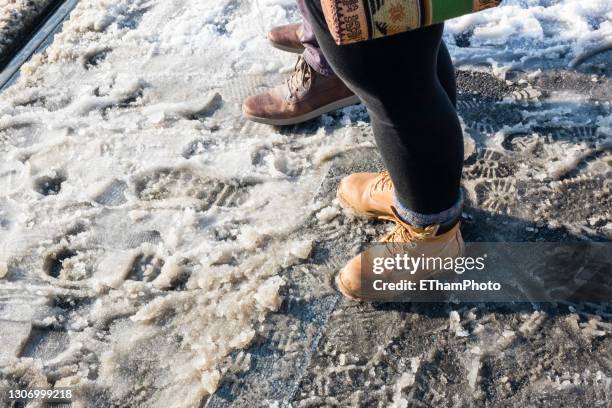 looking down at winter boots and feet of people standing and walking in melting snow and mud (pov) - pov shoes ストックフォトと画像