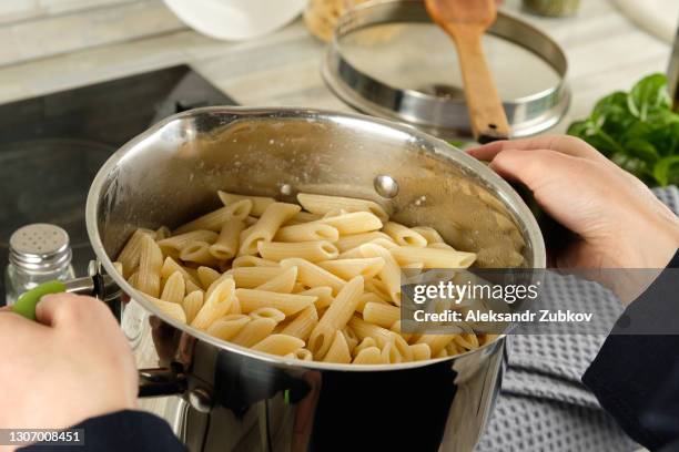 cooking italian pasta, at home. a girl or woman holds a pot of boiled penne paste. vegetarian food. step-by-step instructions, do it yourself. step 4. - rigatoni stock-fotos und bilder