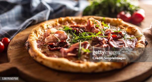 freshly baked pizza with prosciutto, sun dried tomatoes and arugula leaves. - pizza with ham stock pictures, royalty-free photos & images