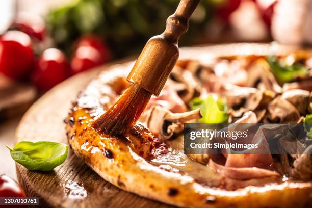 wooden brush spreads olive oil with garlix on the edges of a ham and mushroom pizza. - pizza with ham stock pictures, royalty-free photos & images