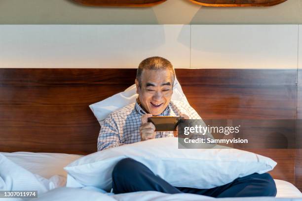 asian man playing mobile game at bedroom - one mid adult man only stock pictures, royalty-free photos & images