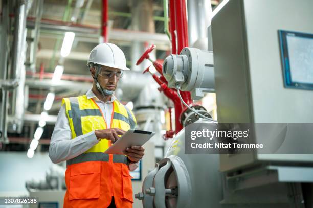 smart professional engineer using touch pad while standing in boiler control room. - boiler engineer stockfoto's en -beelden